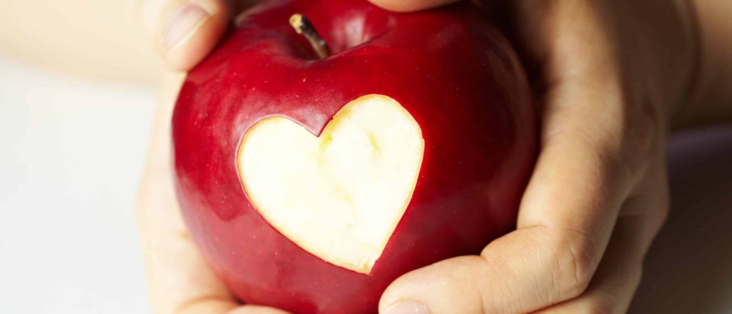 Kädet pitävät punaista omenaa, jota on kuorittu sydämen muotoisen kuvion verran.