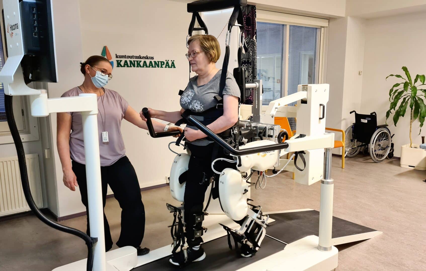 Asiakas harjoittelee Lokomat-kävelyrobotilla ja fysioterapeutti on vierellä.