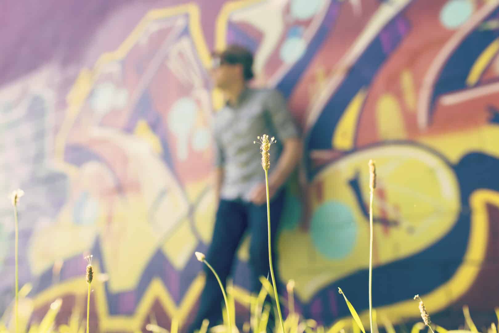 Nuoren elo -kurssin kuvituskuvana nuori mies seisoo seinää vasten, jossa on graffiteja.